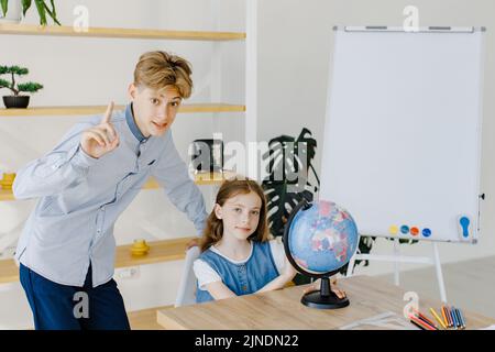 Teenage girl and boy siting near table with globe in classroom. Teen schoolboy and schoolgirl doing project together at school Stock Photo