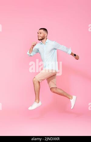 man in summer clothes jumping on pink background. Stock Photo
