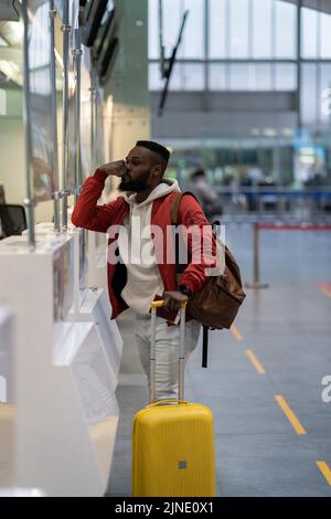 Upset African man standing at check-in counter in airport, being sad about moving away Stock Photo