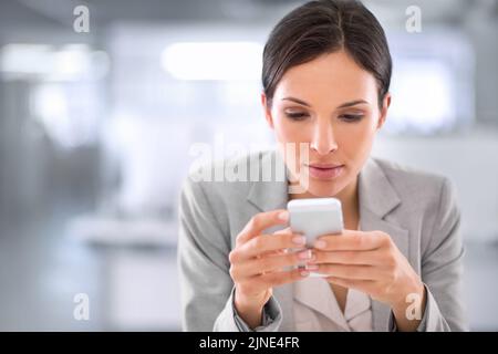 Young woman browsing social media on a phone at work in a modern office. Serious female interested and curious about fake news or stories. Lady Stock Photo