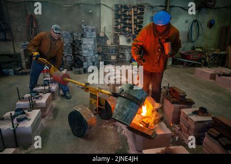 Foundry workers casting molten metal into moulds in a small family foundry in Perth, Western Australia Stock Photo