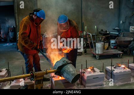 Foundry workers pouring molten metal into moulds  in a small family foundry in Perth, Western Australia Stock Photo