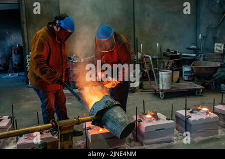 Foundry workers pouring molten metal into moulds  in a small family foundry in Perth, Western Australia Stock Photo