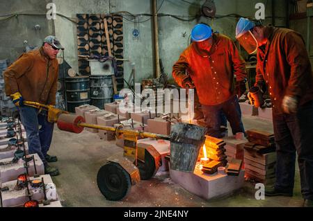 Foundry workers casting molten metal into moulds in small family foundry in Perth, Western Australia Stock Photo