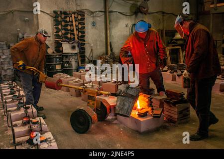 Foundry workers casting molten metal into moulds in small family foundry in Perth, Western Australia Stock Photo