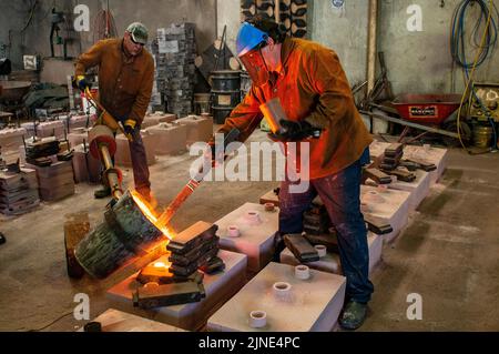 Foundry workers pouring molten metal into moulds  in a small family foundry in Perth, Western Australia Stock Photo