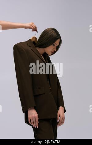 woman holding hanger with teenage model in recyclable blazer isolated on grey Stock Photo