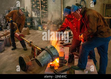 Foundry workers casting molten metal into moulds in small family foundry in Perth, Western Australia Stock Photo