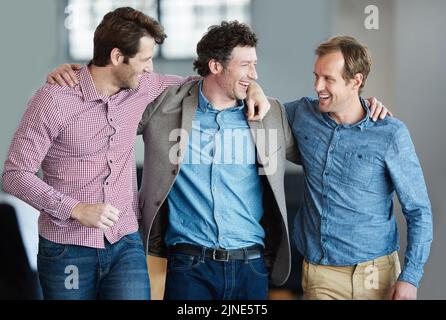 Teamwork, friendship and support with colleagues standing together in a huddle laughing and feeling happy in a creative office. Business men embracing Stock Photo