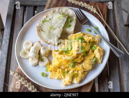 Breakfast plate with scrambled eggs, buttered white bread and bananas. Stock Photo