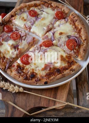 Pizza with ham and cheese, cherry tomatoes and red onions on wooden background Stock Photo