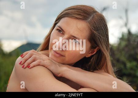 Young woman casual portrait - leaning on her palm and shoulder looking to side, closeup detail, blurred trees background Stock Photo