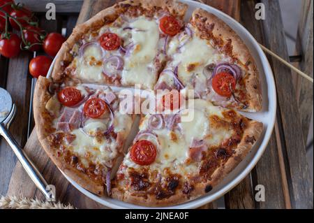 Pizza with ham, mozzarella cheese, red onions and tomatoes on a plate Stock Photo