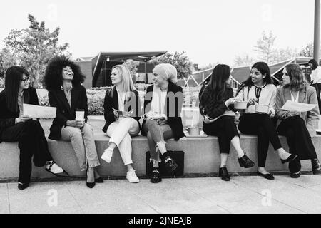 Multiethnic business women doing lunch break outdoor from office building - Focus on blond girl face - Black and white editing Stock Photo