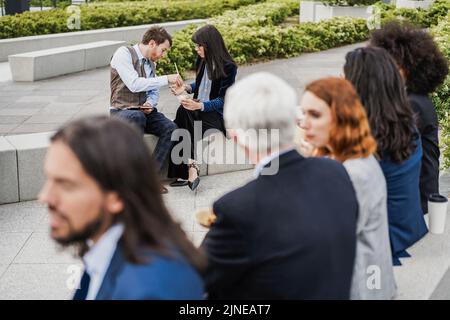 Multiethnic business people doing lunch break outdoor from office building - Focus on bottom couple Stock Photo