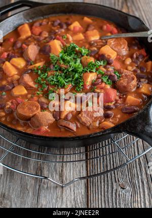 Spicy stew with chorizo sausage, beans, sweet potatoes and vegetable in a cast iron pan Stock Photo