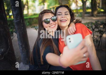 Two female friends posing and taking pictures in a park Stock Photo