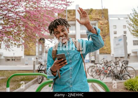 Guy smiling at camera raising hand in greeting Stock Photo