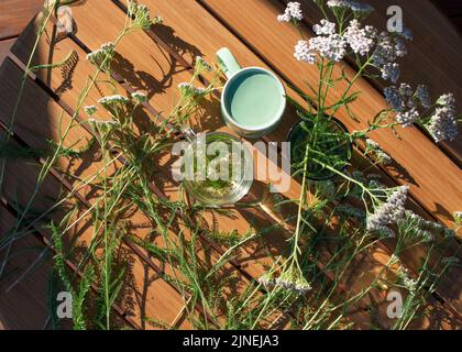 Yarrow plants and glass of yarrow herb tea on wooden table, top view. Stock Photo