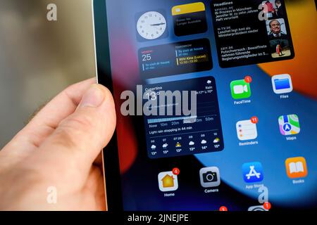Paris, France - Oct 25, 2021: Close-up macro shot of male hand holding latest Apple Computers iPad Mini Pro tablet computer with all apps on display - weather aoom news clock and calendar - tilt-shift lens Stock Photo