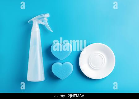 Spray bottle, heart shaped sponges and clean white plate on blue background. Top view. Cleaning concept. Stock Photo