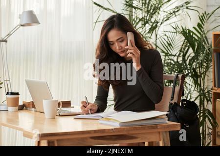 Young woman checking notes in her diary when calling on the phone Stock Photo