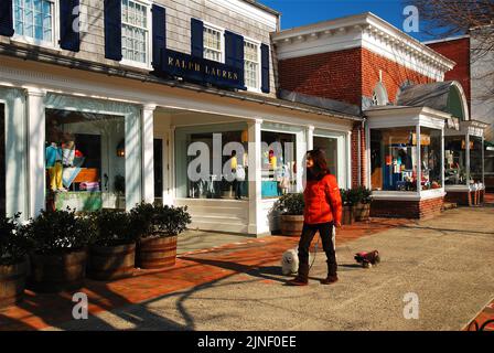 A young woman walks her dogs past the luxury designer stores in East Hampton, Long Island, New York, one of the wealthy towns of The Hamptons Stock Photo