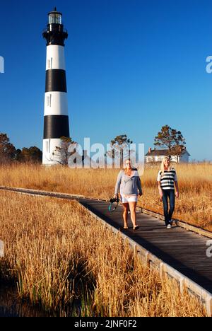 Two women walk on the boardwalk as it travels through a swamp area near the Bodie Island Lighthouse on the Outer Banks of North Carolina Stock Photo