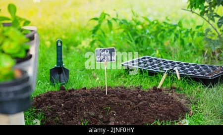Board with go green lettering in soil near gardening tools and grass in garden,stock image Stock Photo