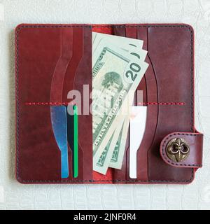 Open red leather clutch with money and credit cards on light leather background. Stock Photo