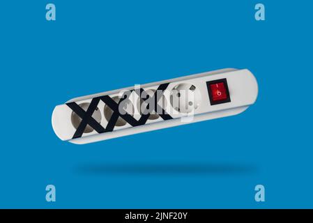 Multi-socket power strip with some of them blocked on blue background. Concept of energy saving or restriction and responsible use of electricity Stock Photo