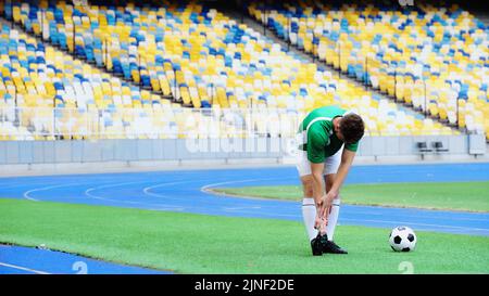 young football player in uniform stretching near ball of green field,stock image Stock Photo