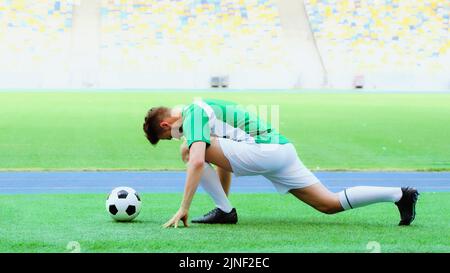 young football player in uniform stretching legs on green grass bear soccer ball,stock image Stock Photo