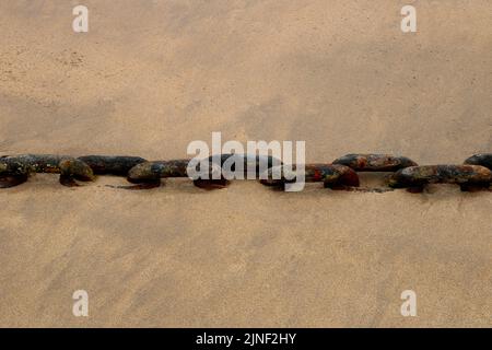 Old rusty heavy duty steel chain half buried at a seafront location Stock Photo