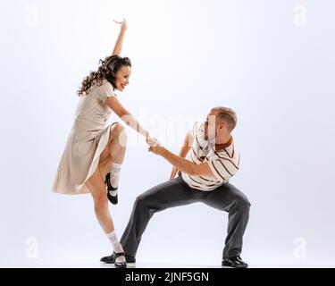 Dynamic portrait of emotional man and woman dancing sport dances isolated on white background. 50s, 60s ,70s american fashion style. Stock Photo