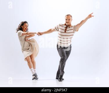 Dynamic portrait of emotional man and woman dancing sport dances isolated on white background. 50s, 60s ,70s american fashion style. Stock Photo