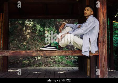 african american man in blue striped shirt and sneakers sitting in wooden patio,stock image Stock Photo