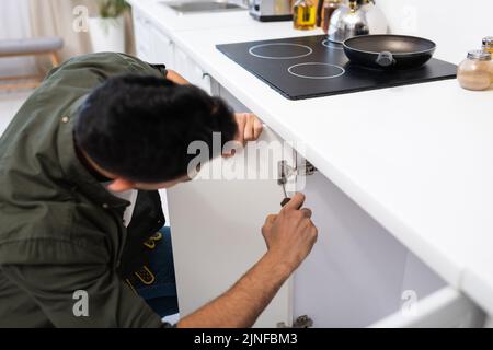Blurred craftsman with screwdriver fixing metal hinge in kitchen cabinet,stock image Stock Photo
