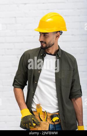 Smiling muslim man in hardhat and gloves touching tool belt at home,stock image Stock Photo