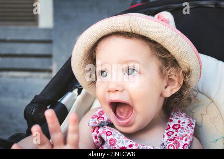 A cute white Caucasian little girl wearing a round straw summer hat looking surprised and happy Stock Photo