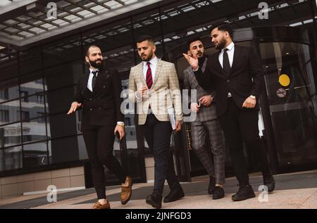 Business people outdoor meeting, A group of male businessmen in suits exit the front door of a glass building. Working break. Teamwork and Stock Photo