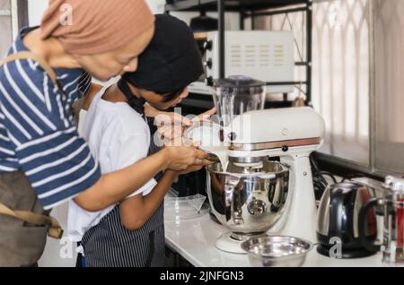 Mother teaching her son baking cake by pouring milk into a mixing bowl. Stock Photo