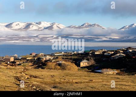 Traditional small village on the shore of the paravani lake with beautiful snowy mountains in the background, Javakheti Volcanic Plateau, Georgia Stock Photo