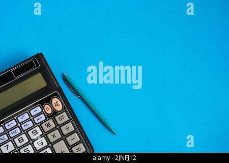 Calculator turned off and a ballpoint pen on blue background Stock Photo