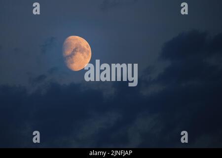 Bright orange moon against dark sky and clouds Stock Photo