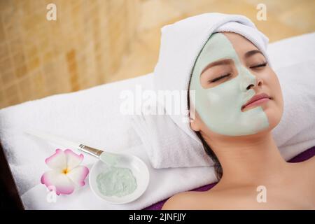 Beautiful Asian young woman lying with clay mask on half on her face Stock Photo