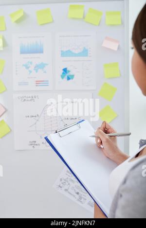 Business woman looking at board with various graphs and diagrmans to draw conclusion on progress of work Stock Photo