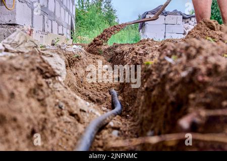 Construction worker is digging trench for laying cables, using shovel to excavate soil. Stock Photo