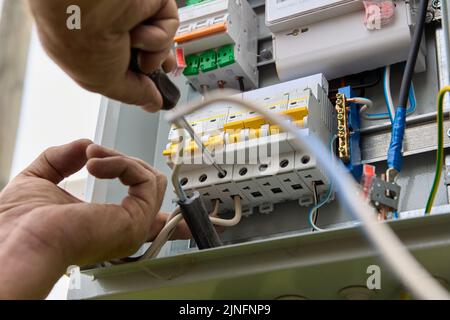 Fastening circuit breakers to DIN rail of consumer unit of electrical panel. Mounting fuse box for distribution board. Stock Photo