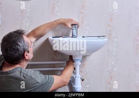 Plumbing work on installing new water faucet in toilet, plumber is tightening nut that secures tap to surface of washbasin. Stock Photo